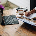 shot of female accounting bookeeper providing accounting service for small businesses, sitting at desk with portable computer, holding pen to make notes and using calculator, woman using digital tablet and calculator.